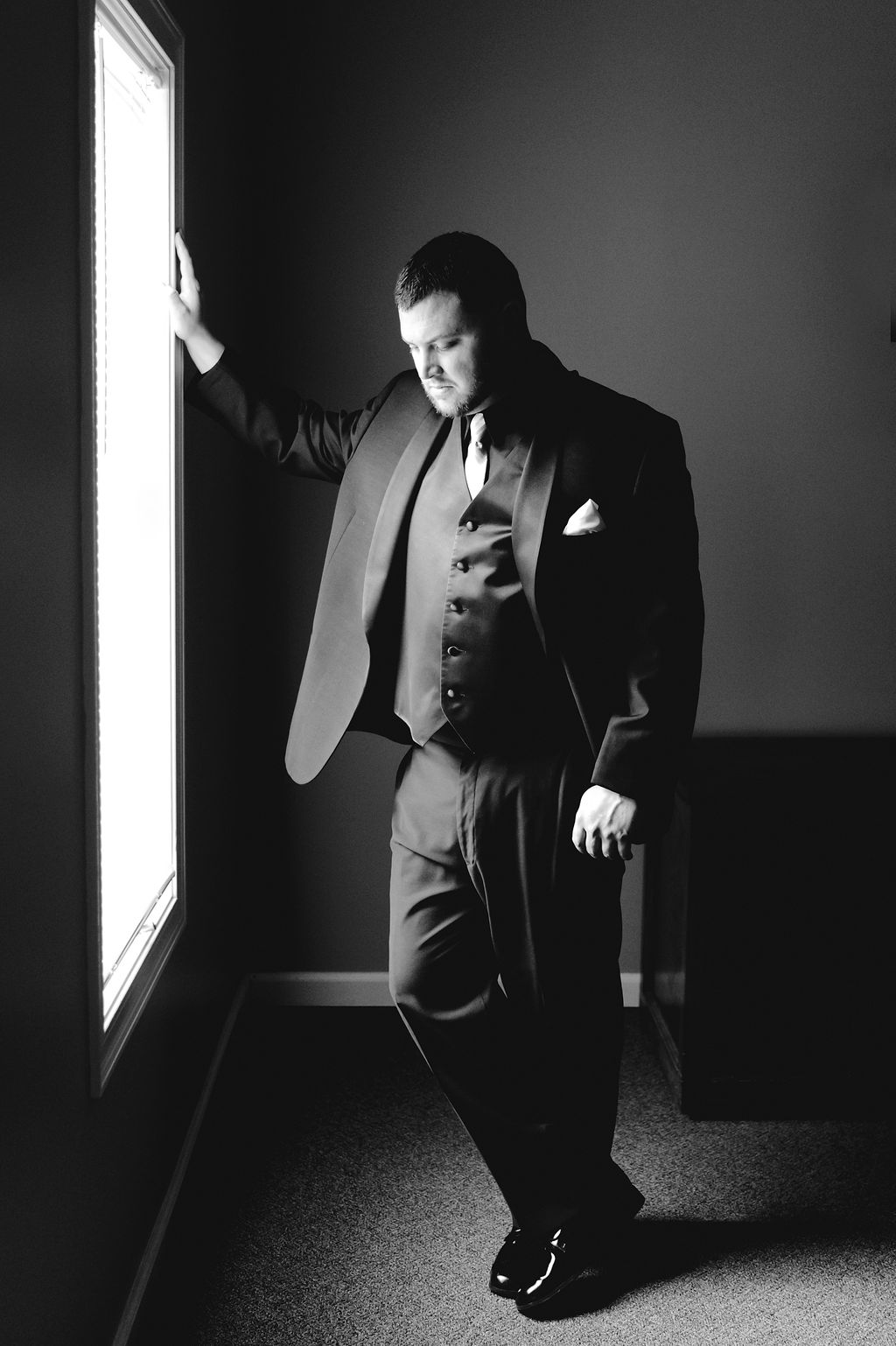 Groom poses next to window looking away from the camera