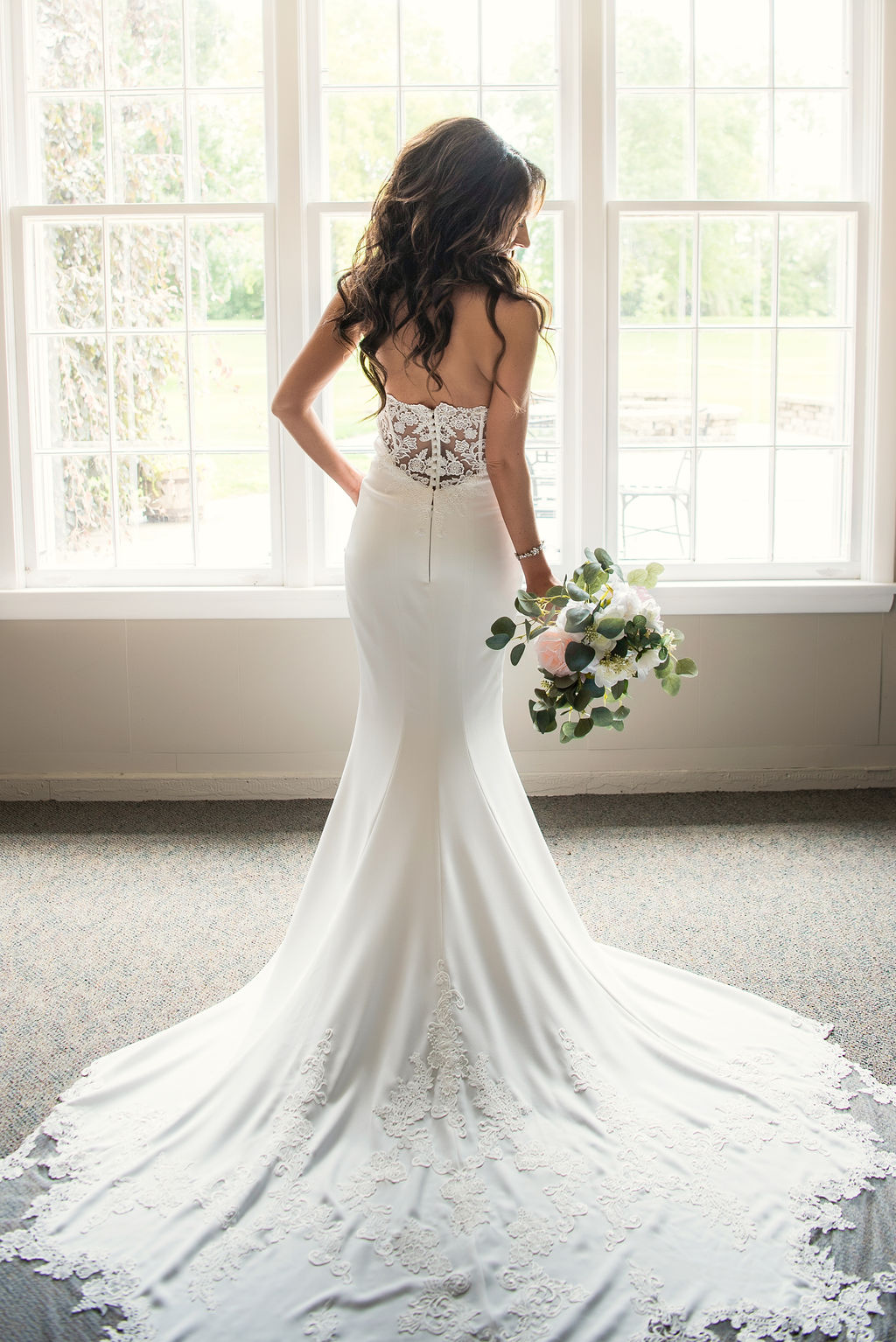 Bride stands in front of bright and airy windows holding her bouquet