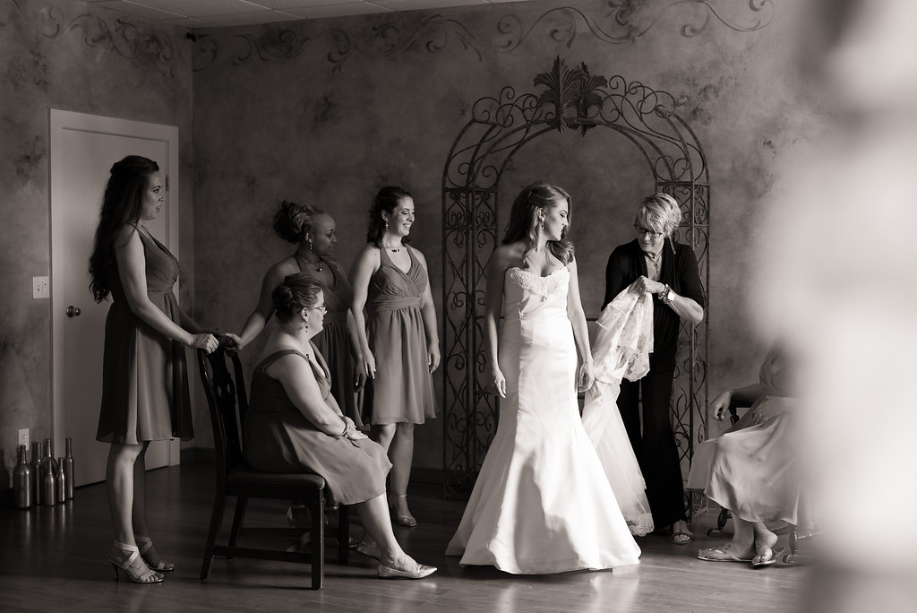 black and white image of bride surrounded by bridesmaids while mother fluffs her gown | tips for choosing a getting ready space