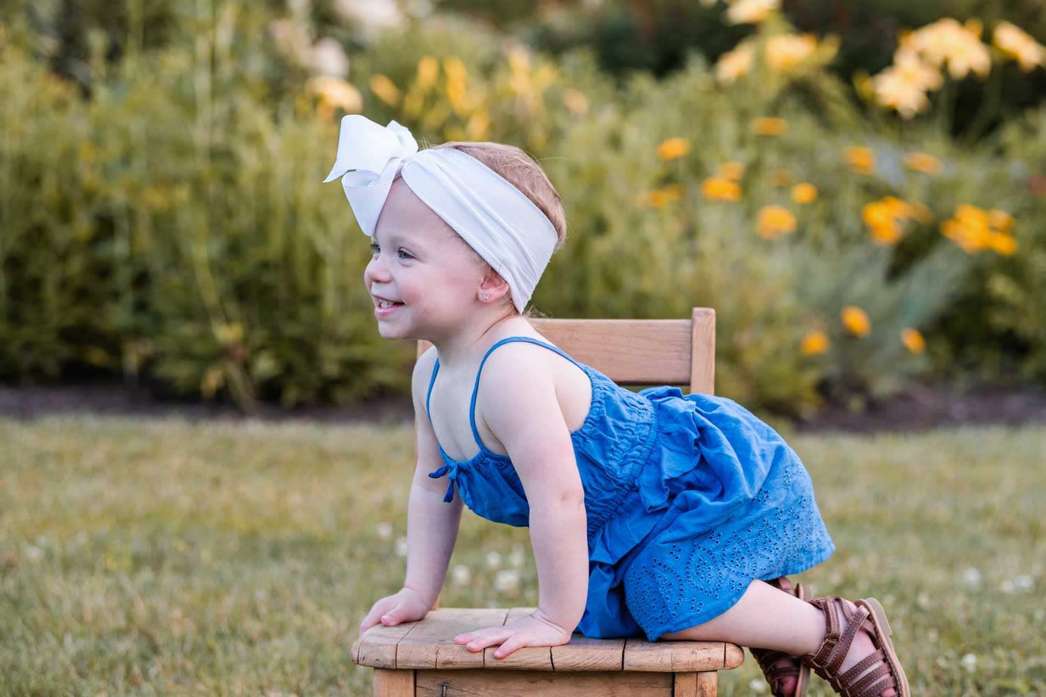 Toddler girl sitting on a chair smiling with white bow in her hair